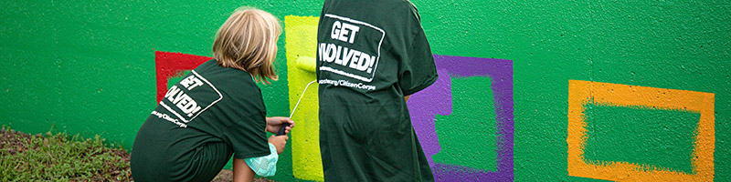 Girls paint over graffiti in a public space.